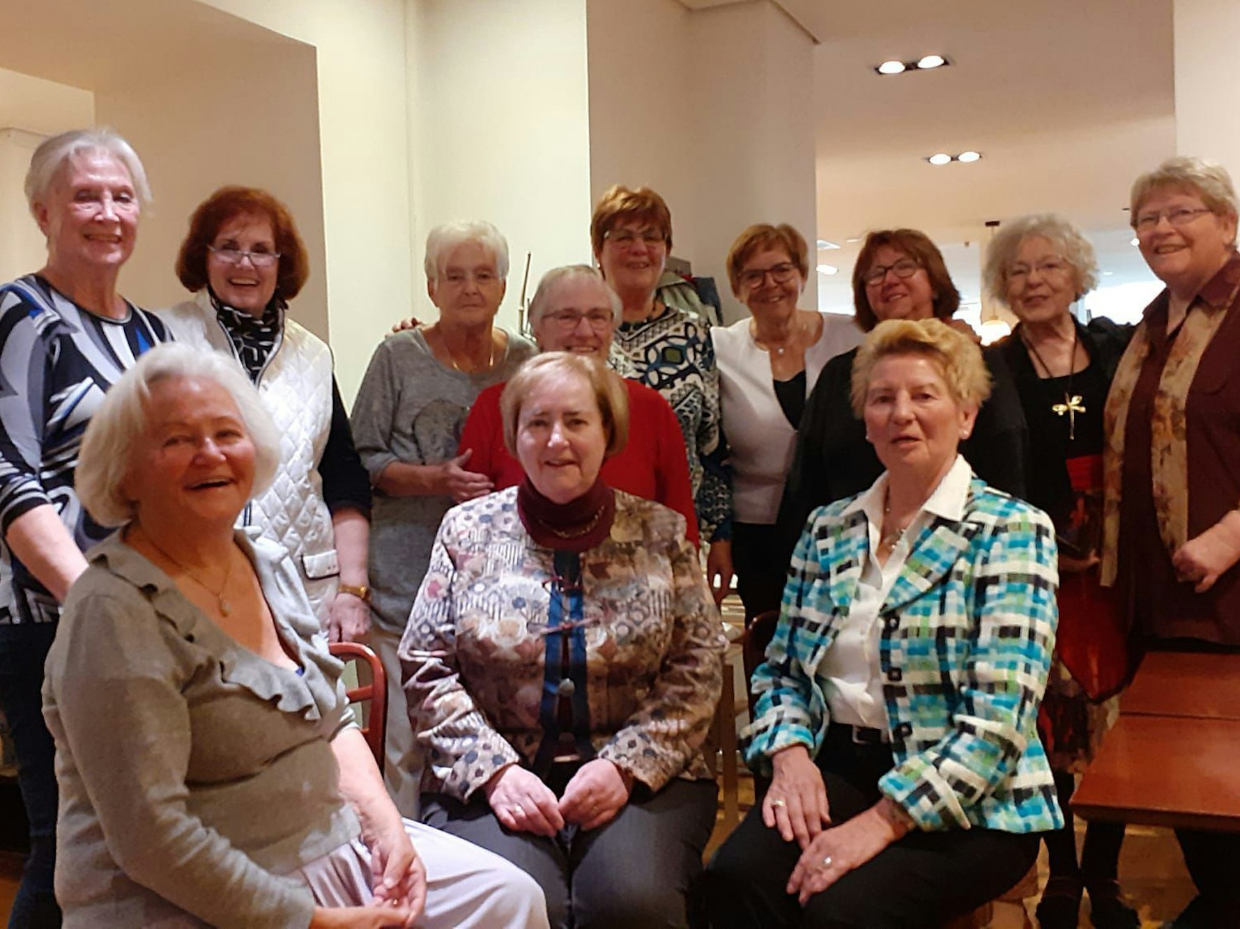 Zwölf ältere Damen posieren gemeinsam für ein Gruppenfoto.
