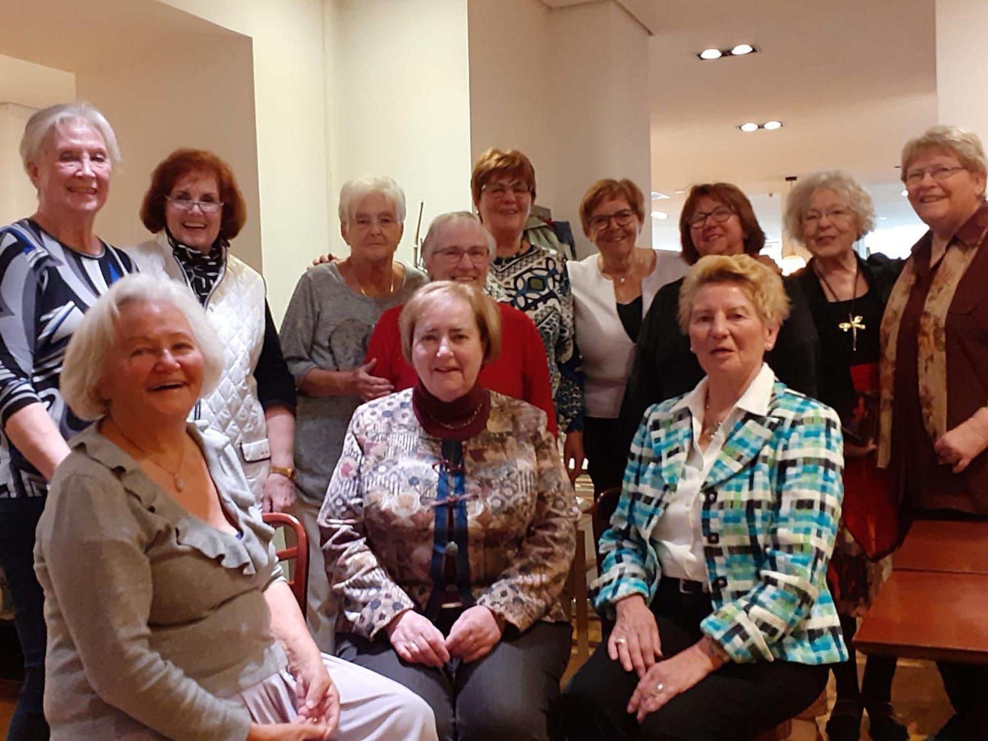 Zwölf ältere Damen posieren gemeinsam für ein Gruppenfoto.