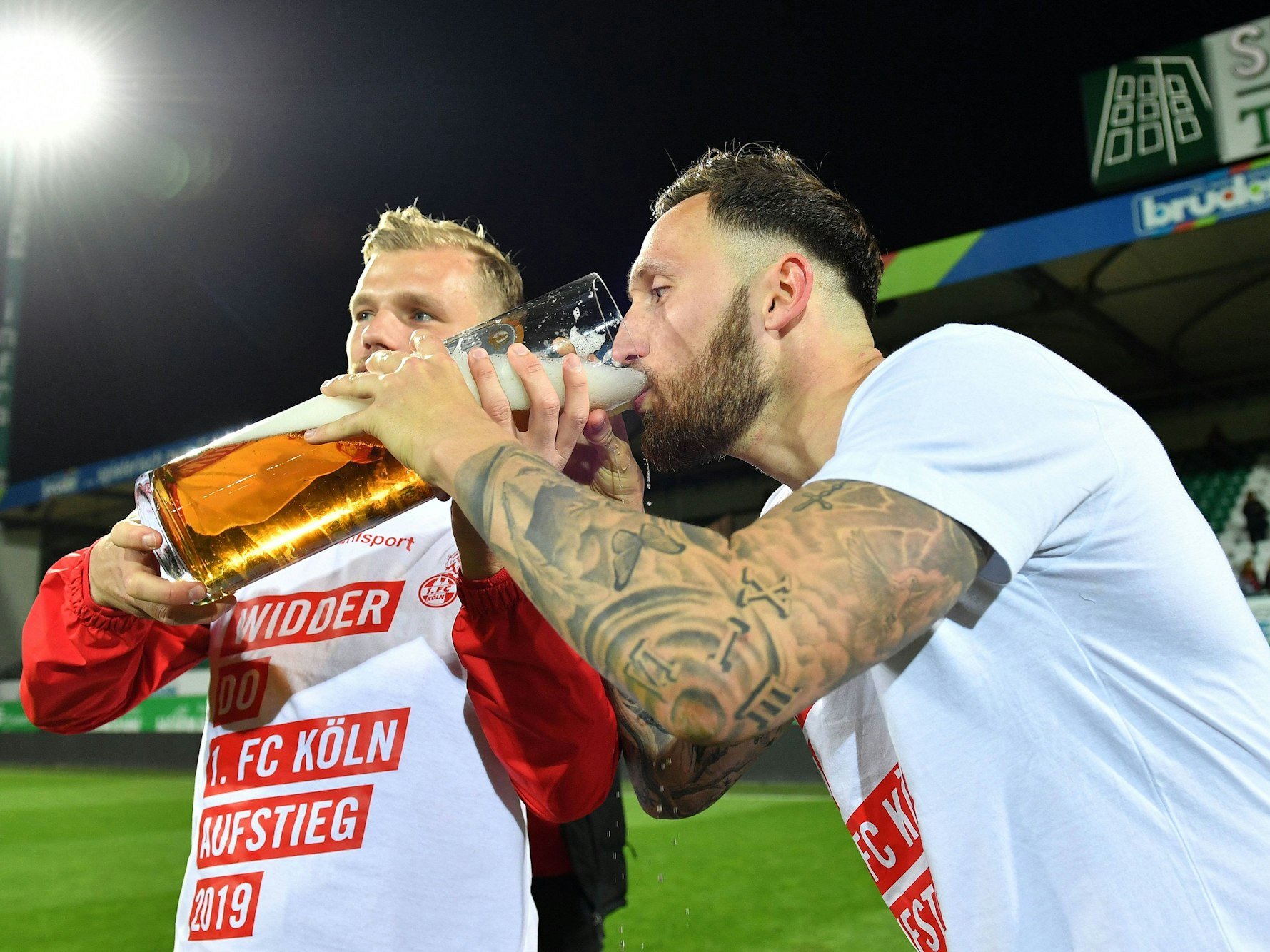Johannes Geis und Marco Höger trinken nach dem Aufstieg aus einem XXL-Kölschglas.