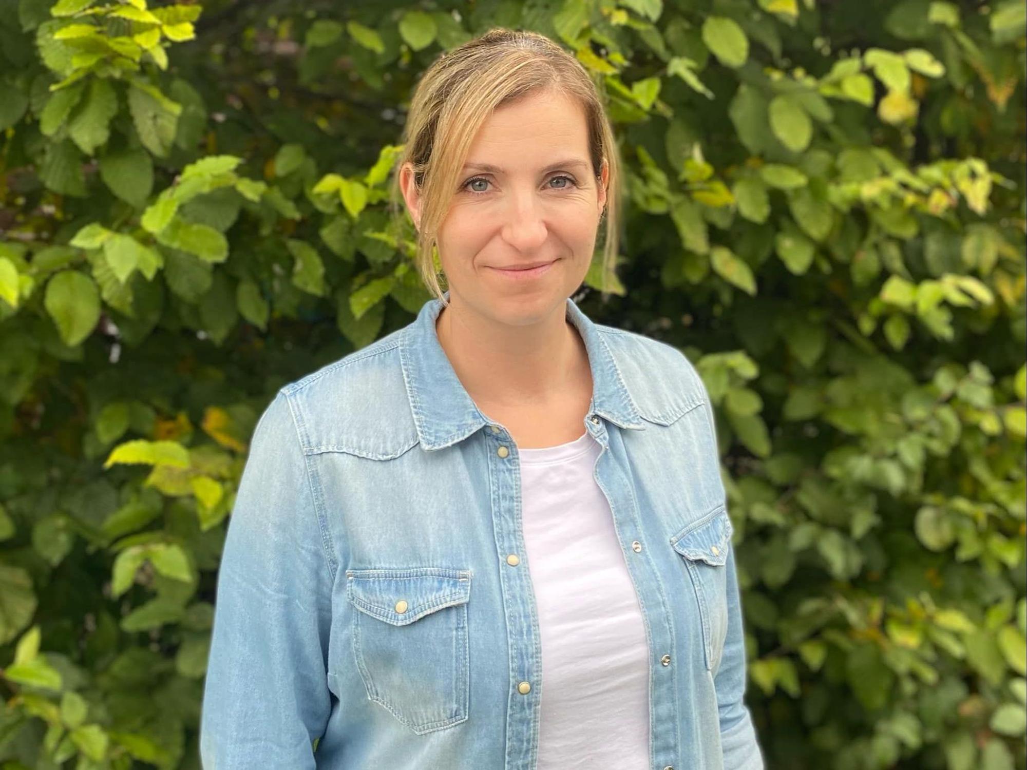 Eine Frau steht vor einer Hecke.