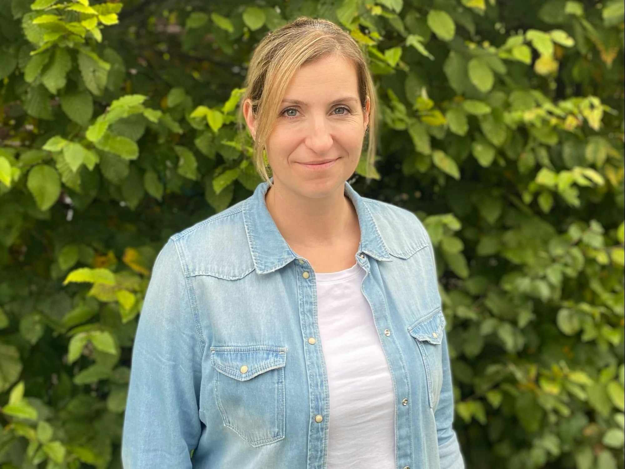 Eine Frau steht vor einer Hecke.