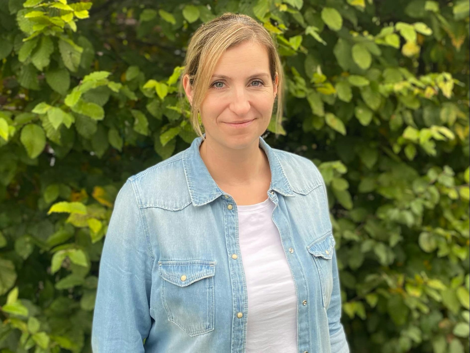 Eine Frau steht vor einer Hecke.