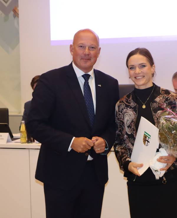 Eine Frau hält einen Blumenstrauß und eine Urkunde in der Hand, neben ihr steht ein Mann.