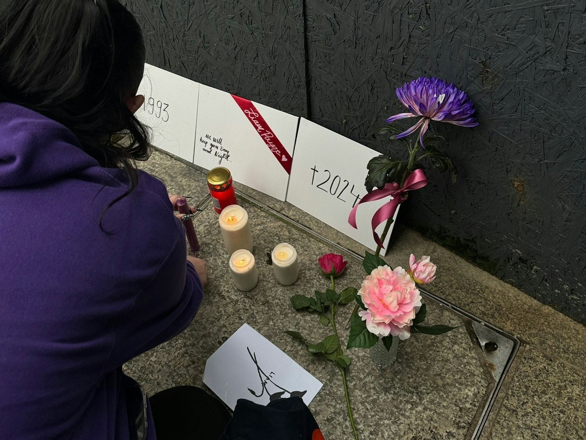 Eine Person kniet vor Blumen und Kerzen.