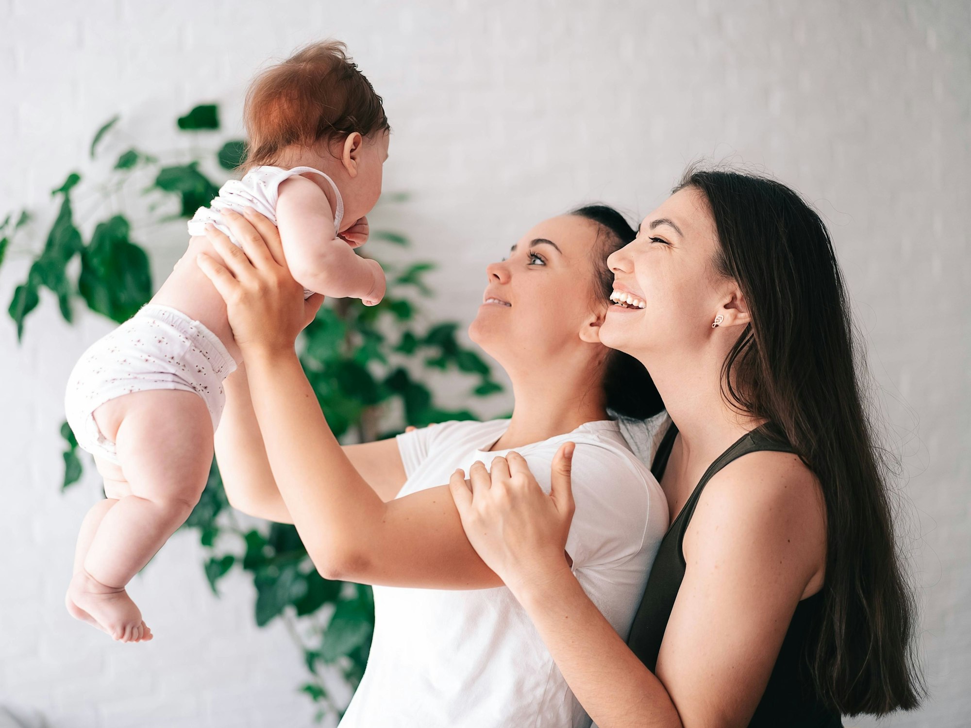 Zwei Frauen halten ein Baby in die Luft und strahlen es an.