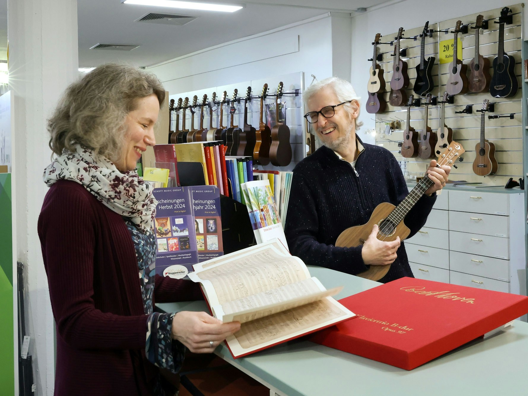 Matthias und Astrid Hinz stehen in ihrem Musikladen und grinsen sich an. Im Hintergrund sind diverse Gitarren und andere Instrumente zu sehen.
