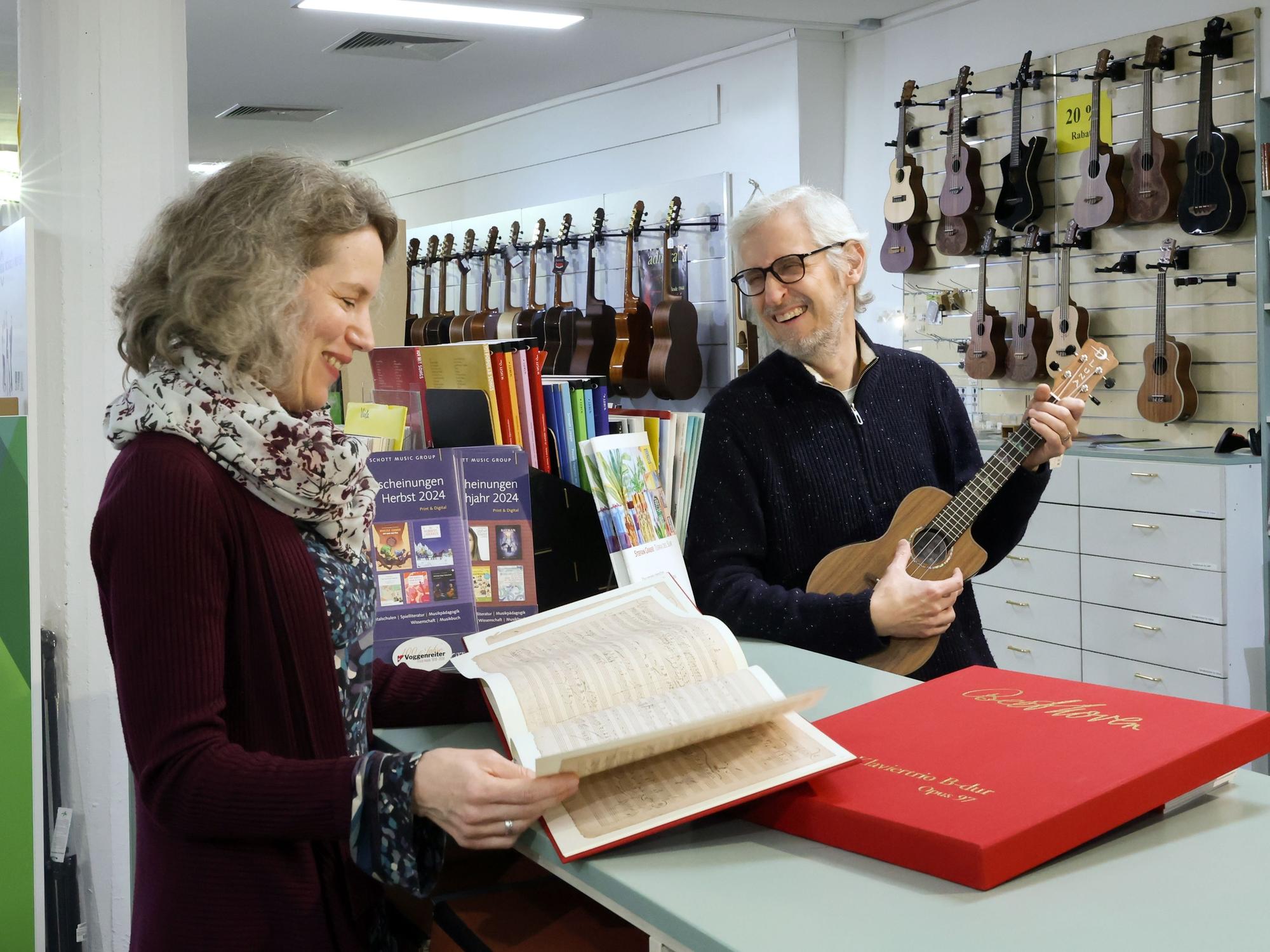 Matthias und Astrid Hinz stehen in ihrem Musikladen und grinsen sich an. Im Hintergrund sind diverse Gitarren und andere Instrumente zu sehen.