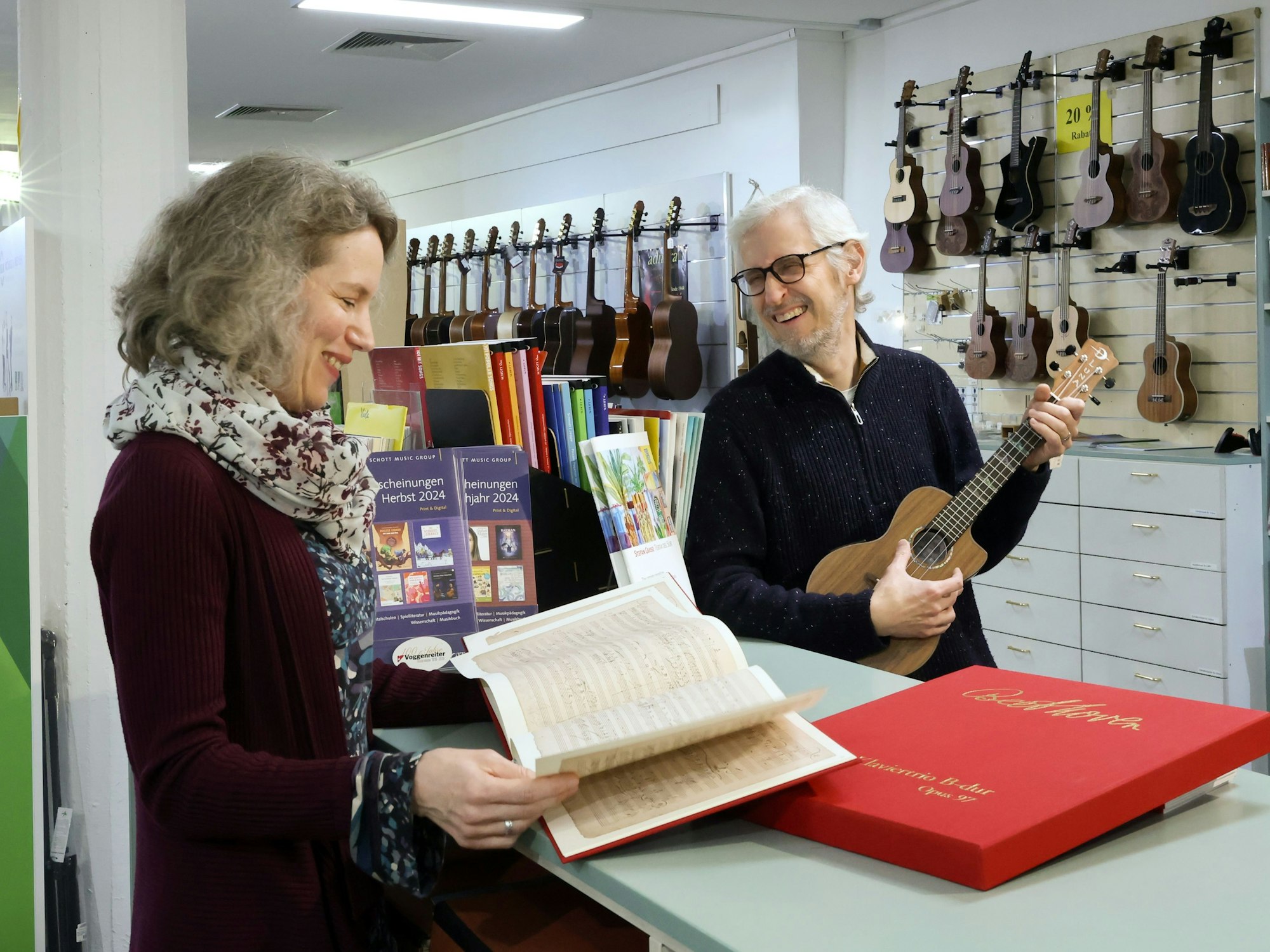Matthias und Astrid Hinz stehen in ihrem Musikladen und grinsen sich an. Im Hintergrund sind diverse Gitarren und andere Instrumente zu sehen.