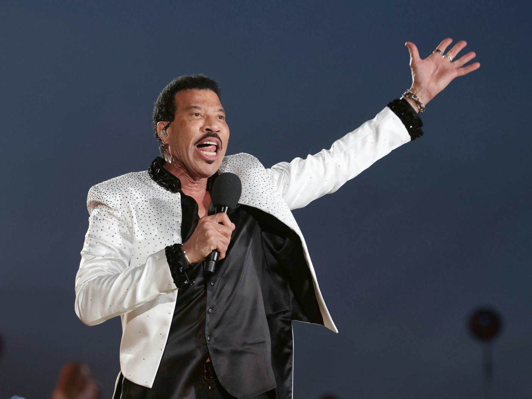 Lionel Richie in weißem Anzug auf der Bühne bei einem Konzert.
