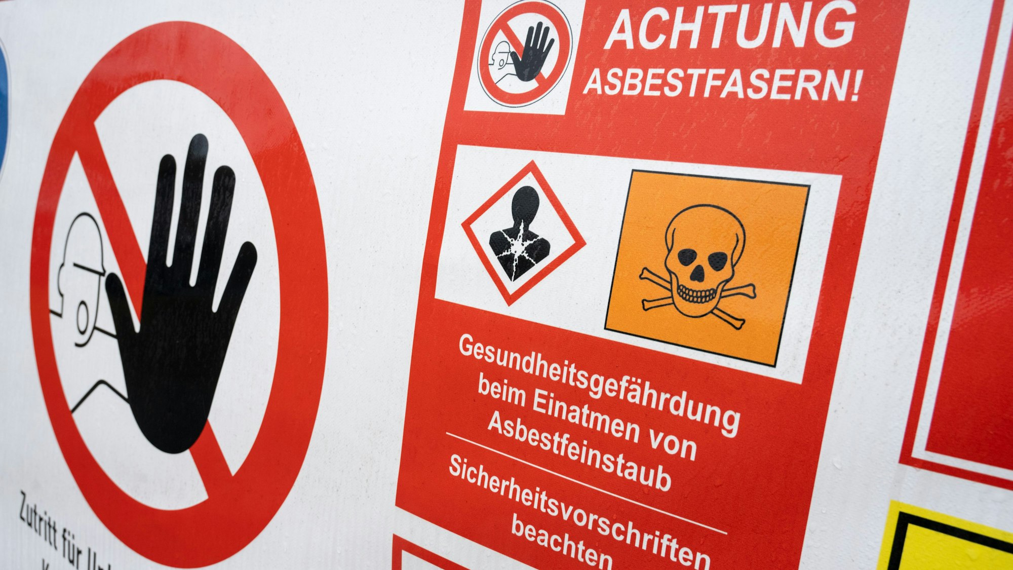 Ein Schild mit der Aufschrift „Achtung Asbestfasern“ hängt an einem Bauzaun.