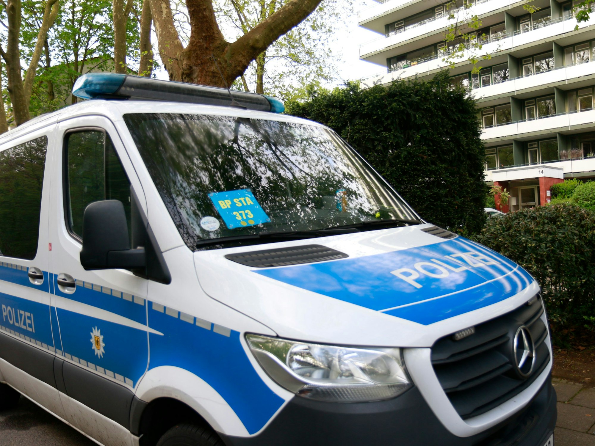 Ein Einsatzfahrzeug der Kölner Polizei steht vor einem Mehrfamilienhaus.