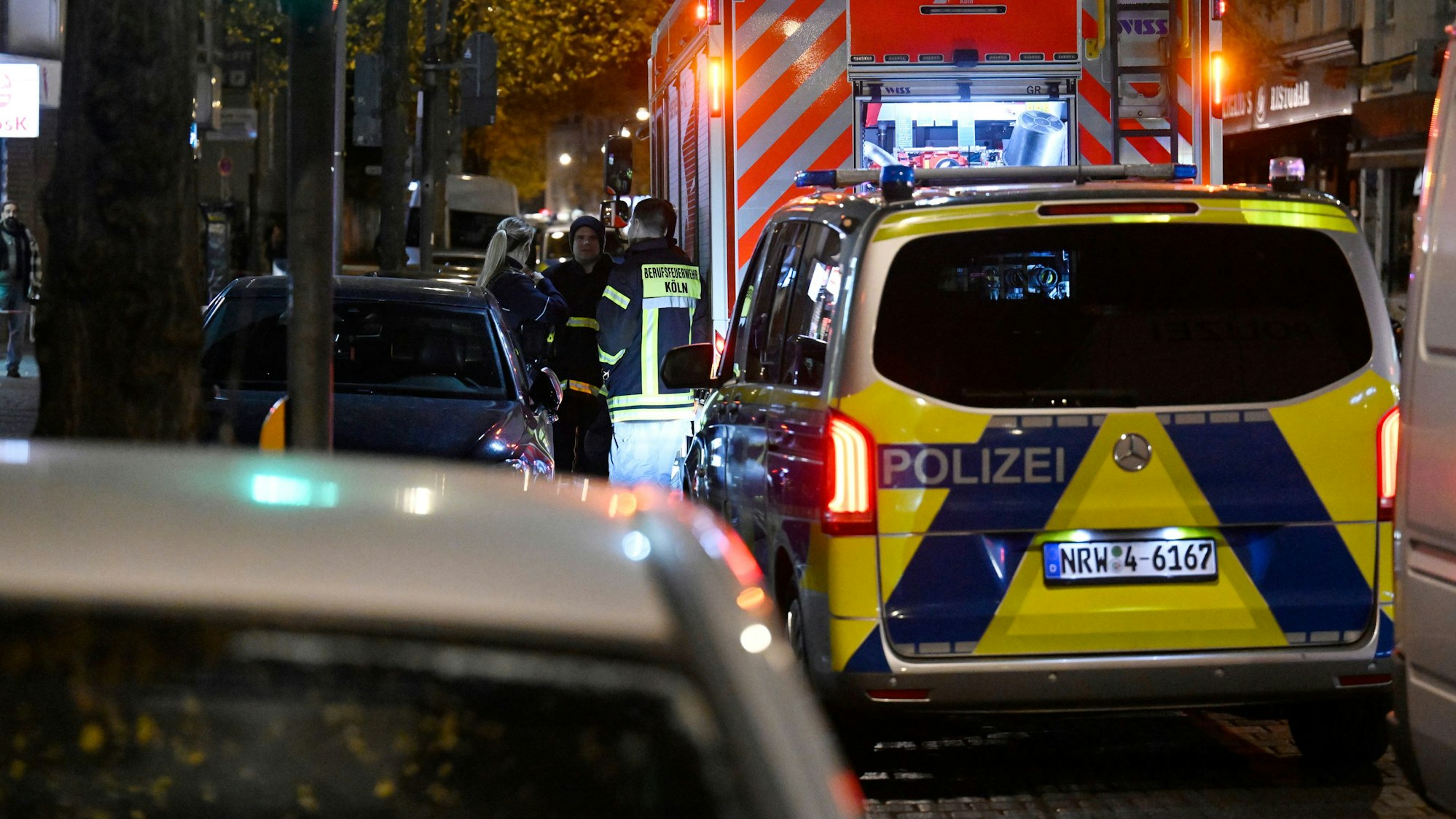Polizei- und Feuerwehrwagen stehen an einem Tatort im Stadtteil Ehrenfeld. Am Donnerstagabend sind zwei Männer durch Schüsse schwer verletzt worden. Die Polizei wurde wegen einer Schlägerei gerufen und hat vor Ort die verletzten Männer gefunden. +++ dpa-Bildfunk +++