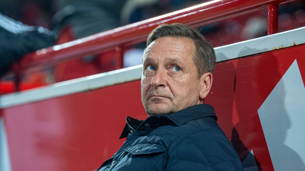 Horst Heldt sitzt auf der Trainerbank.