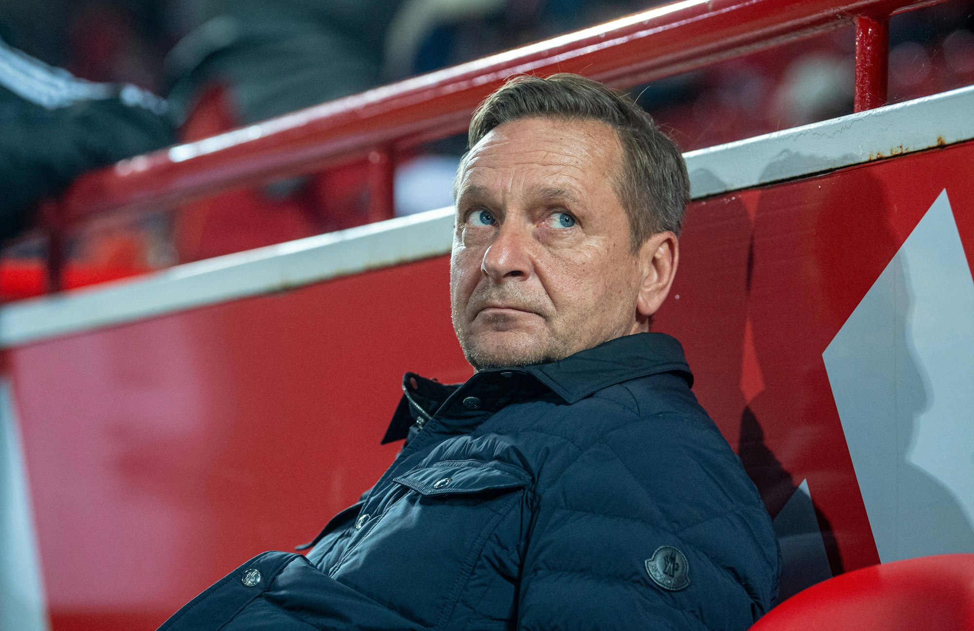 Horst Heldt sitzt auf der Trainerbank.