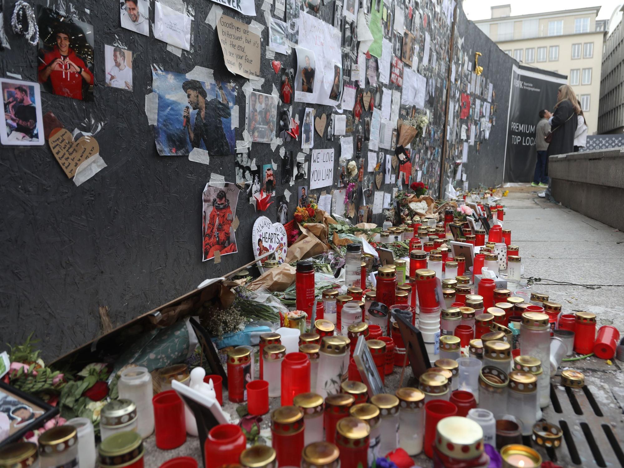 An einer Wand hängen unzählige Fotos und Herzchen, davor steht ein Meer aus Kerzen, liegen zahlreiche Blumen.