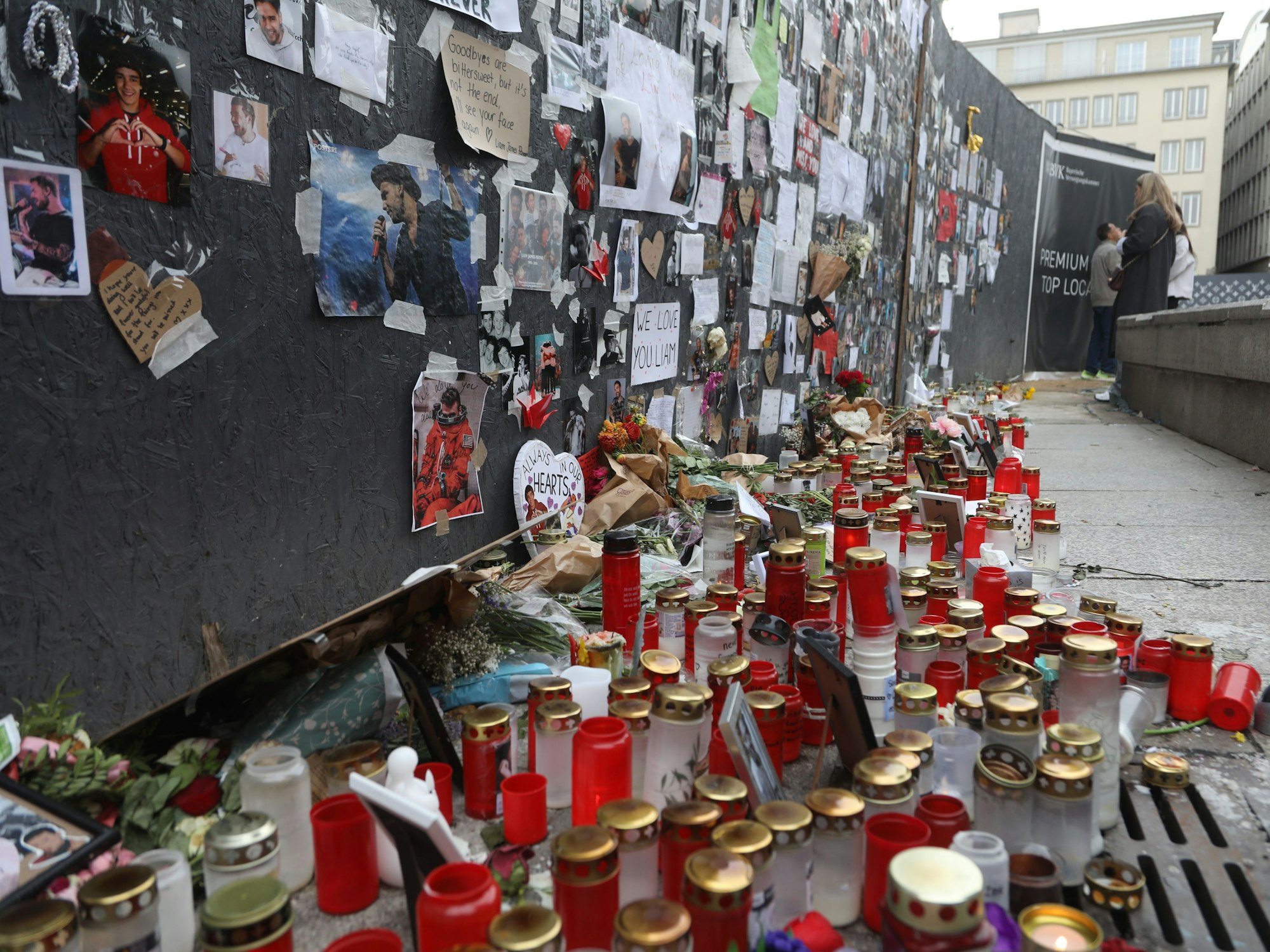 An einer Wand hängen unzählige Fotos und Herzchen, davor steht ein Meer aus Kerzen, liegen zahlreiche Blumen.
