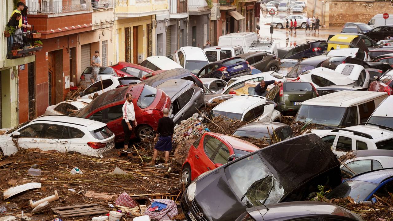 Anwohnerinnen und Anwohner in Valencia (Spanien) betrachten durch die Wassermassen aufgestapelte Autos.