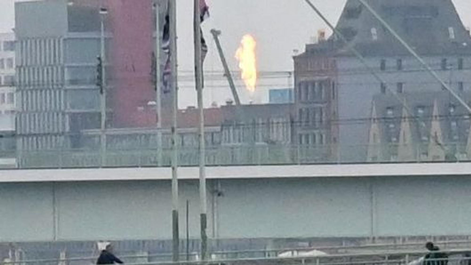 Von einer Brücke aus sieht man zwischen Häusern eine hohe Stichflamme.
