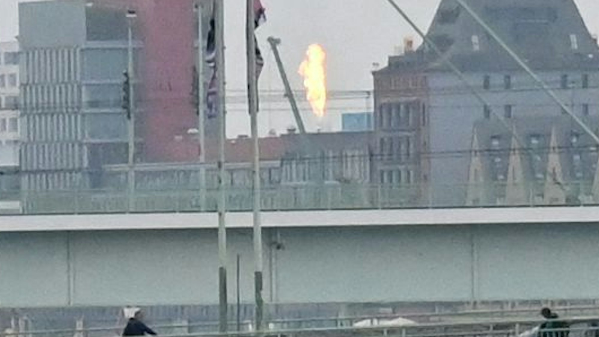 Von einer Brücke aus sieht man zwischen Häusern eine hohe Stichflamme.