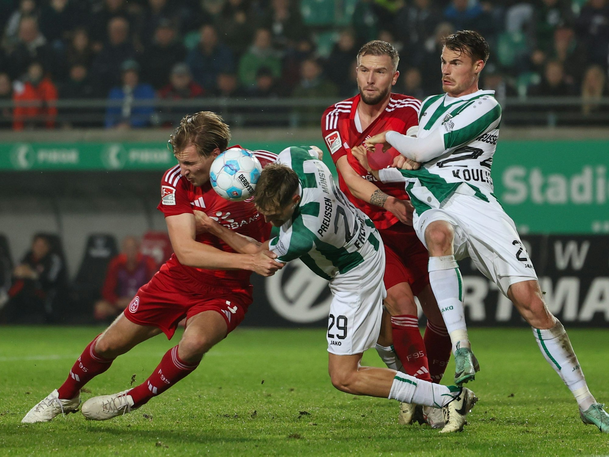 Münsters Lukas Frenkert (2.v.l) und Niko Koulis (r) im Kampf um den Ball mit Düsseldorfs Vincent Vermeij (l) und Andre Hoffmann (2.v.r).