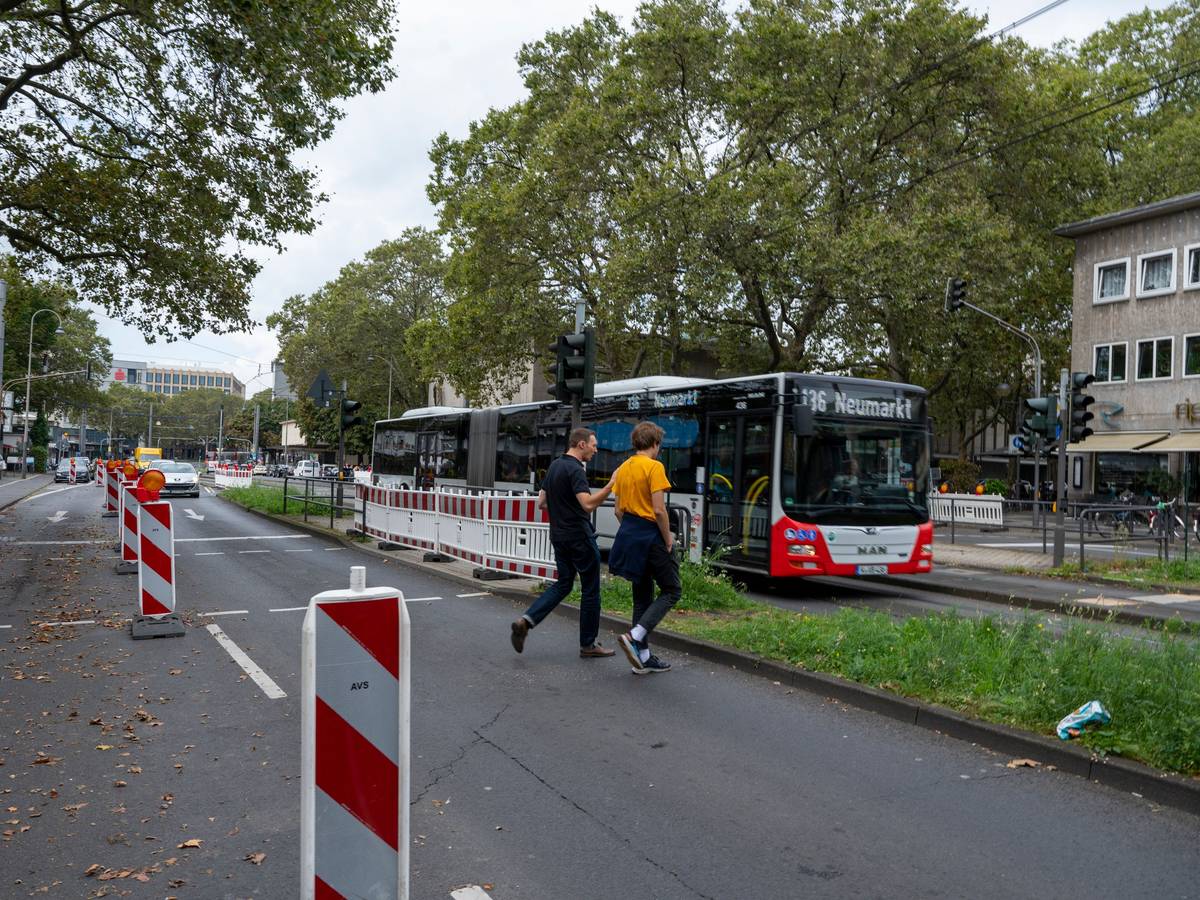 Zwei Männer gehen über eine Ampel, im Hintergrund sind Autos und ein Bus auf der Straße zu sehen.
