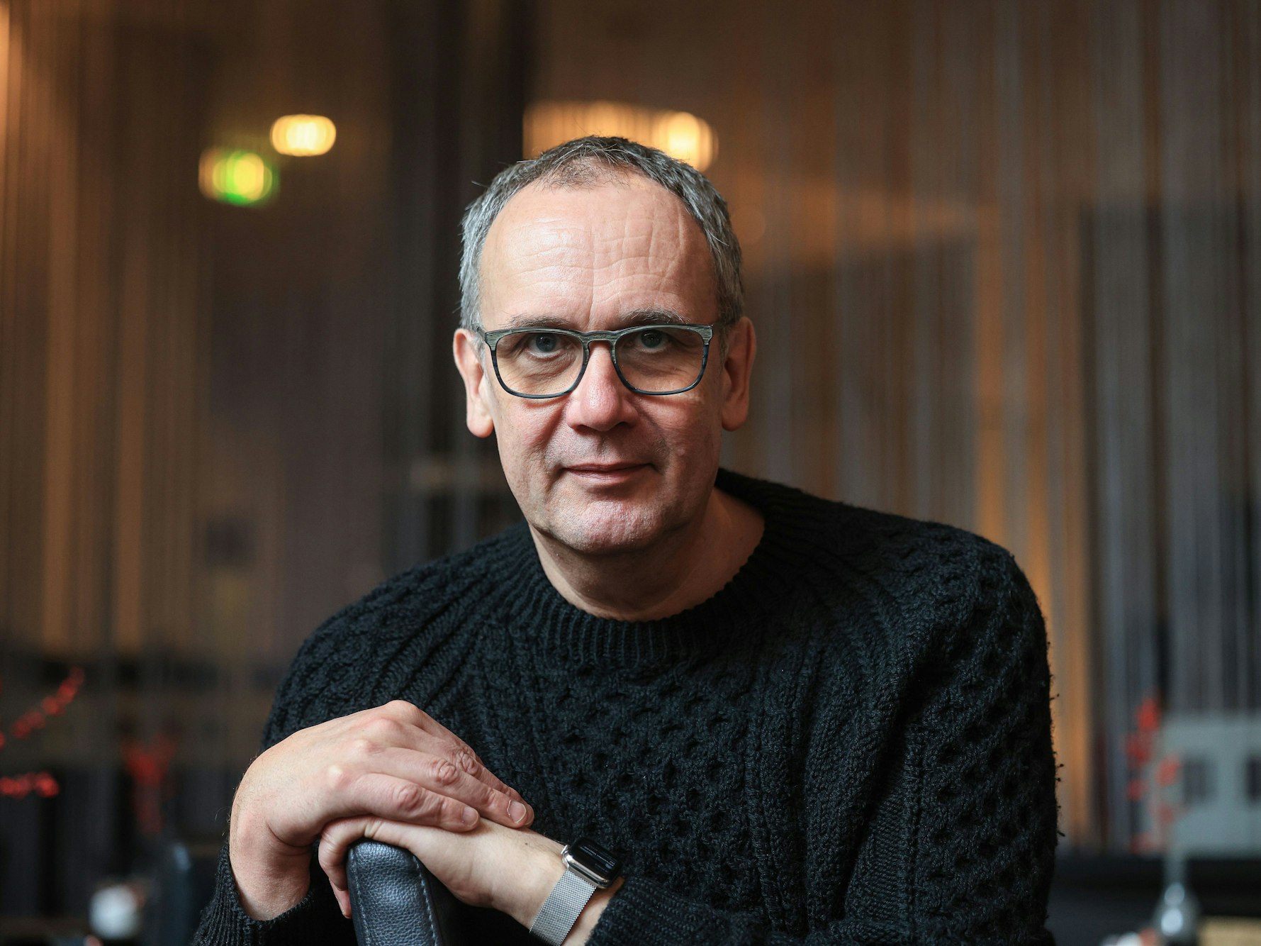 Volker Kutscher sitzt in einem Café in Köln und lächelt leicht in die Kamera.