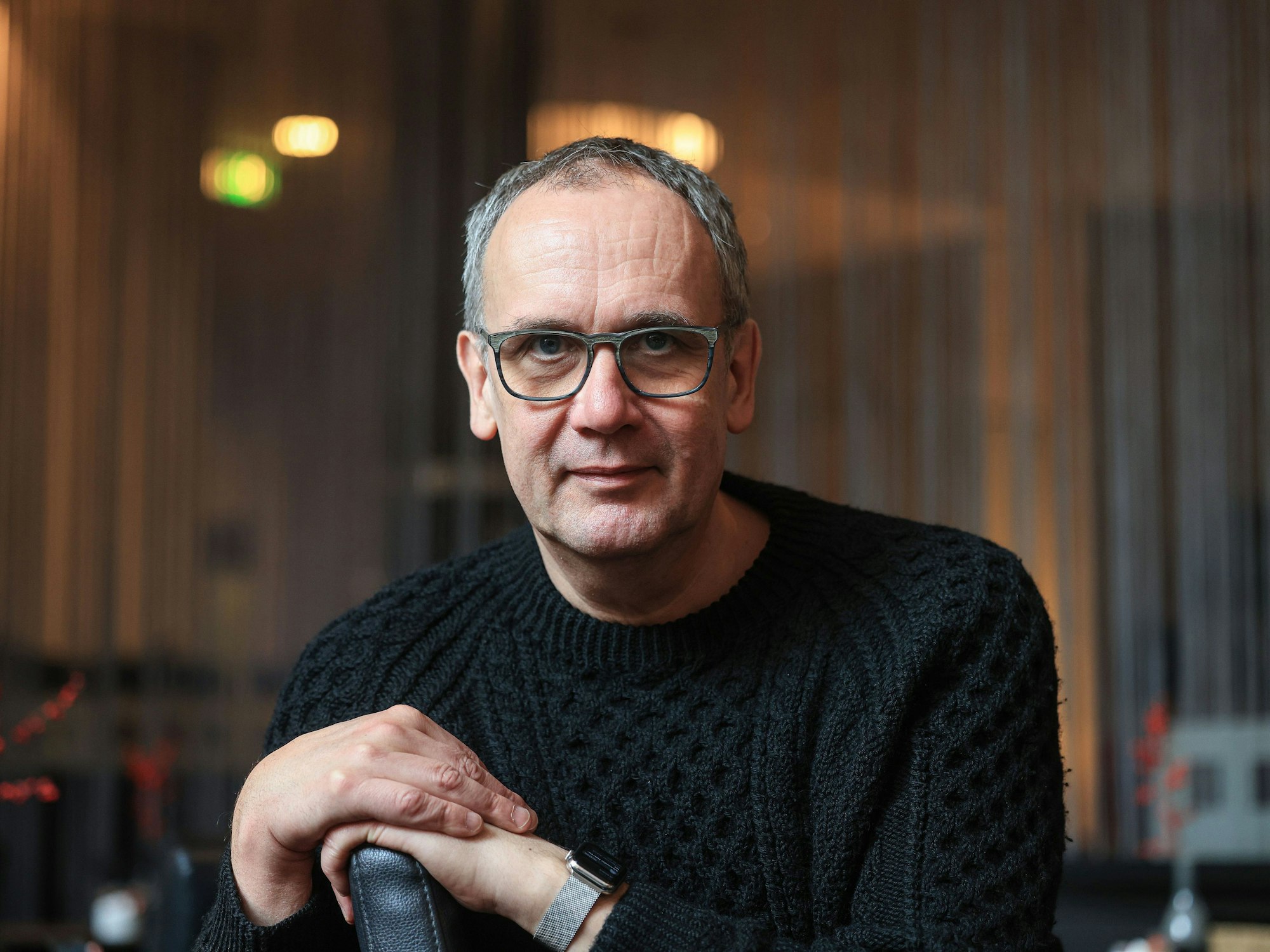 Volker Kutscher sitzt in einem Café in Köln und lächelt leicht in die Kamera.