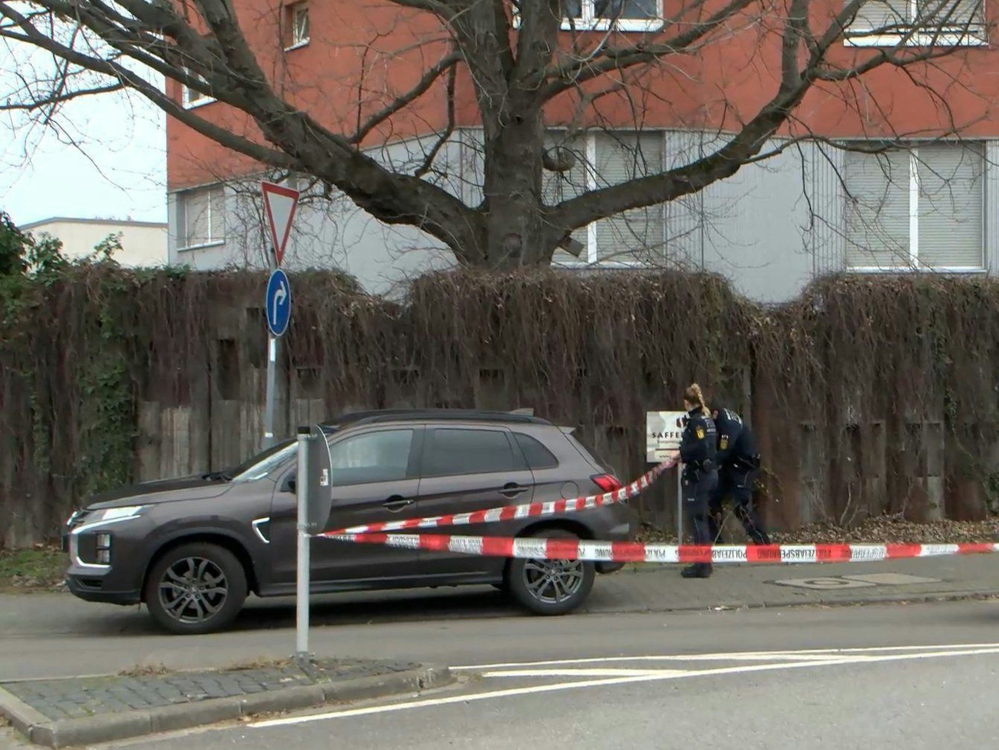 Ein Auto steht auf einer Straße, im Hintergrund bringen Einsatzkräfte der Polizei Absperrband an.