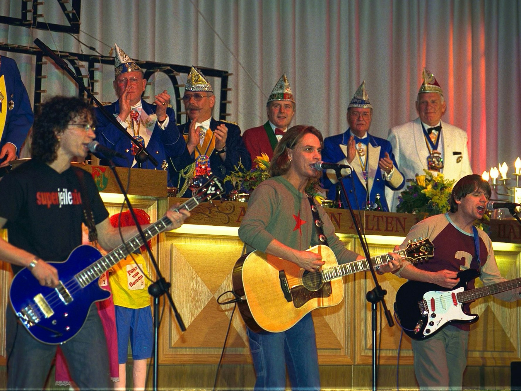 Die Band Brings spielt in einer Reihe auf der Bühne. Im Hintergrund der Elferrat.