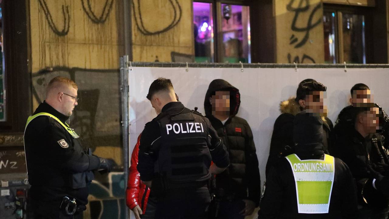 Ein Polizist kontrolliert einen Jugendlichen, der neben weiteren Jugendlichen an einer Absperrung steht. Neben dem Polizisten stehen zwei Kräfte des Ordnungsamtes.