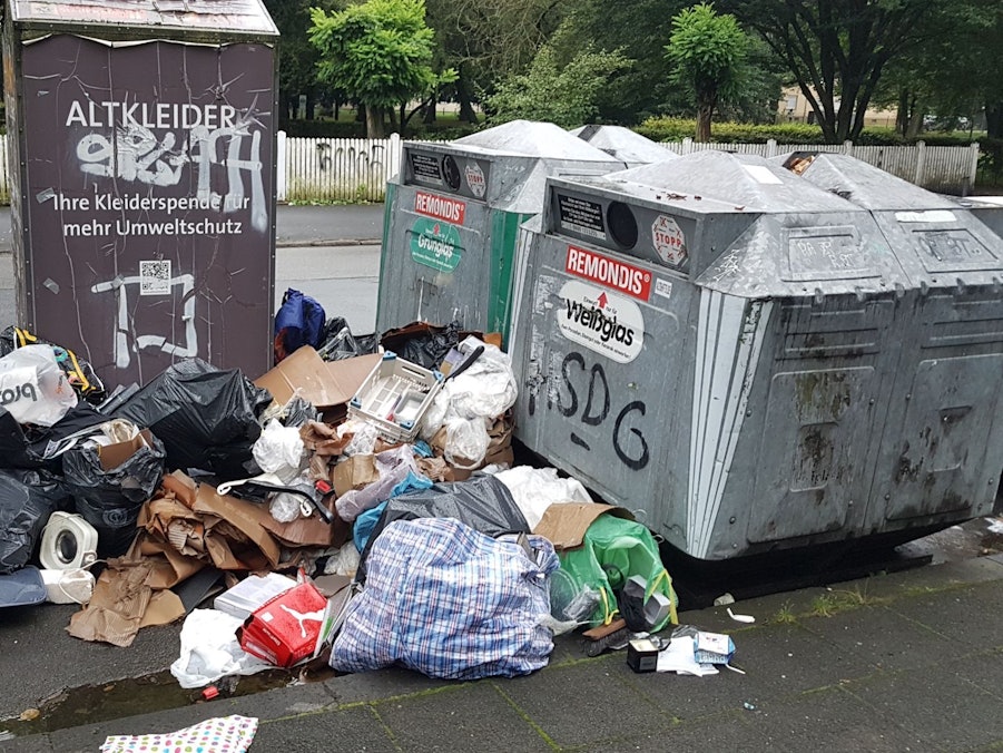Müll steht neben einem Altkleidercontainer und zwei Glascontainern.
