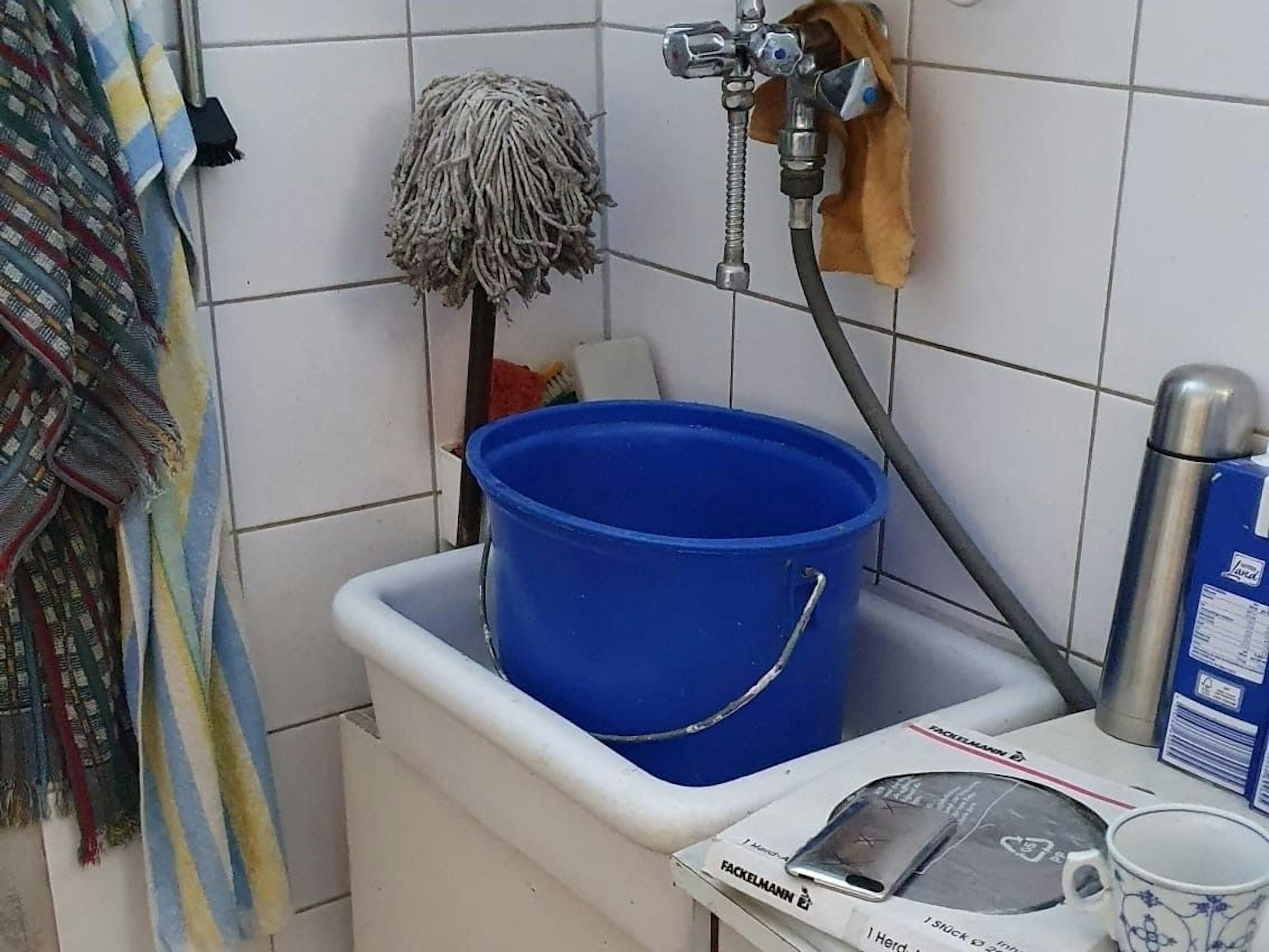 In einem Spülbecken steht ein Eimer, daneben ein Wischmopp.