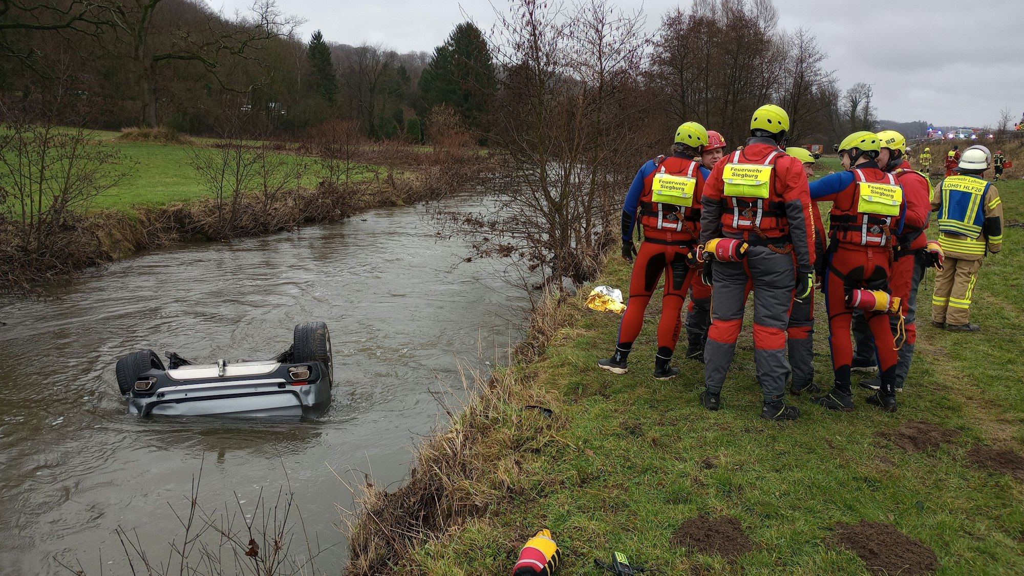 Feuerwehrleute stehen neben einem Auto im Fluss Sülz.