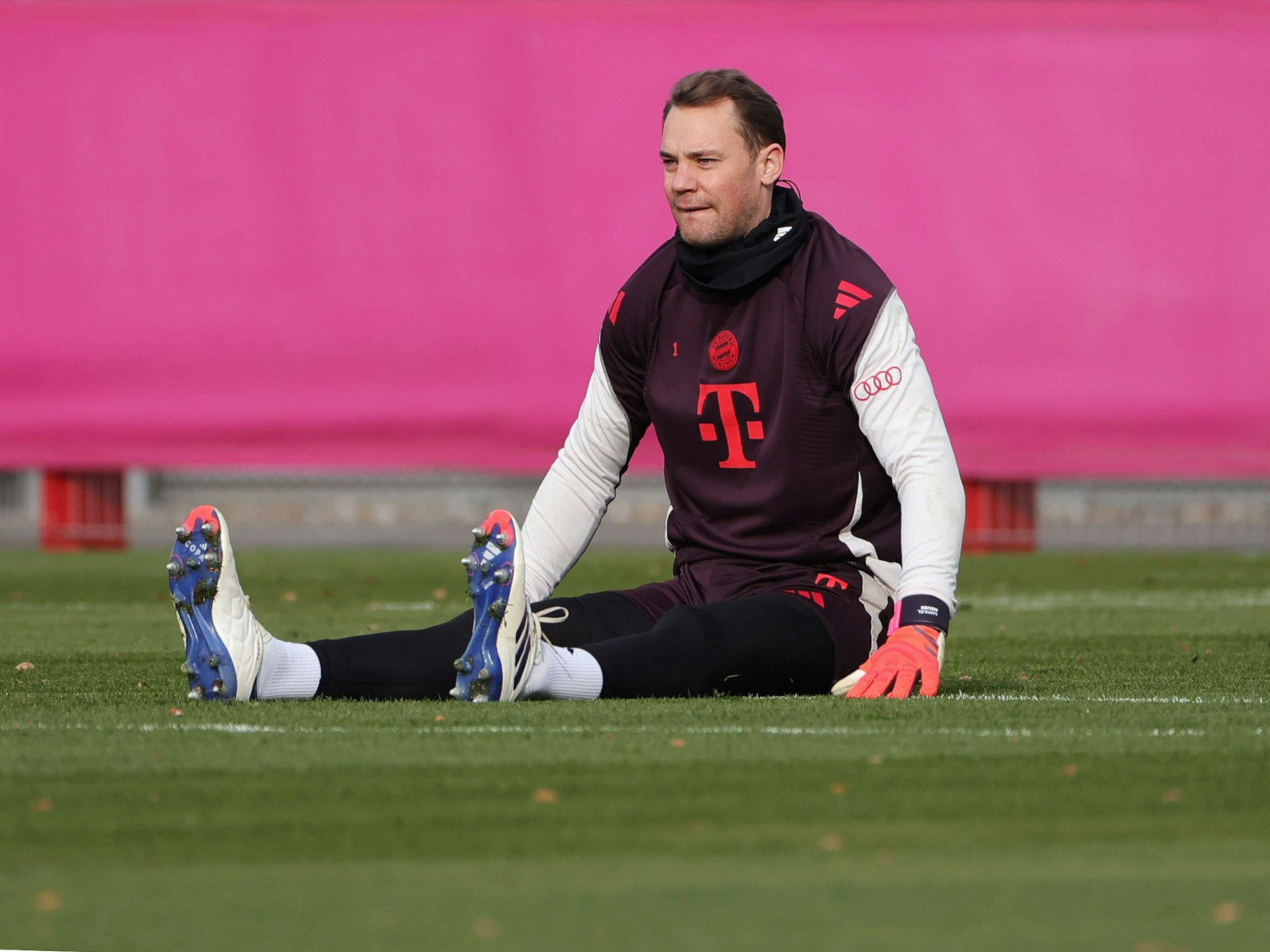 Manuel Neuer sitzt während dem Warmmachen vor dem Training auf dem Rasen.