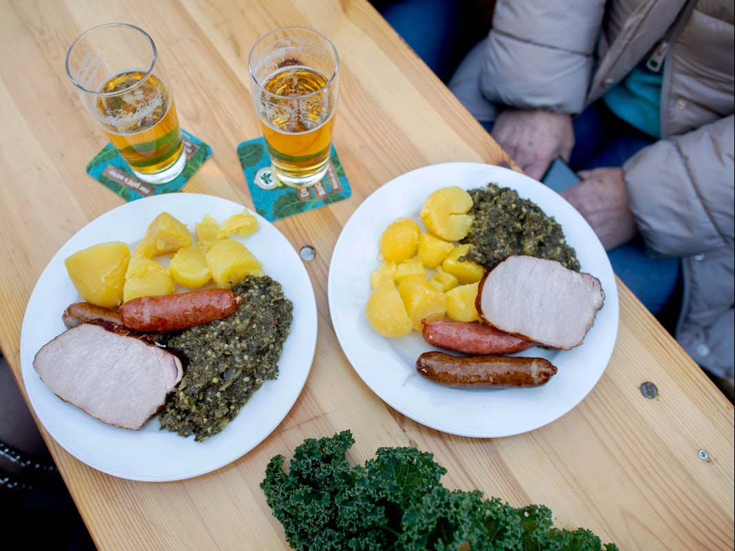 Zwei Teller mit einer Portion Grünkohl und den Beilagen Salzkartoffeln, Kochwurst, Pinkelwurst und Kasseler stehen auf einem Tisch auf dem Rathausmarkt (Symbolbild).