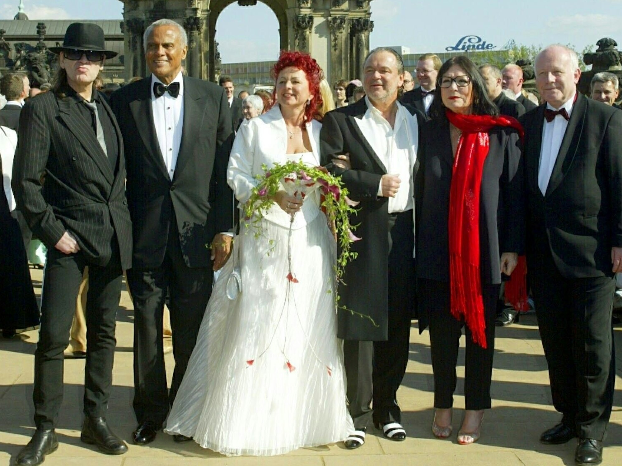 Mehrere Menschen in Anzügen und eine Braut im Hochzeitkleid posieren für ein Foto.
