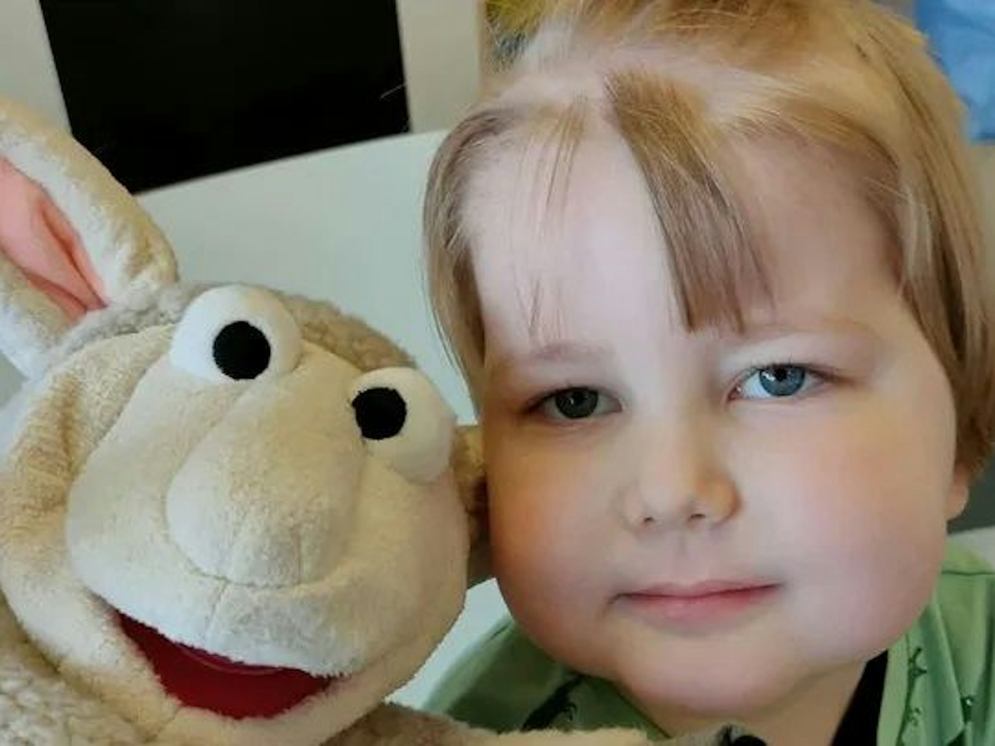 Ein Junge lehnt seinen Kopf an den Kopf eines Plüschtieres mit langen Ohren.