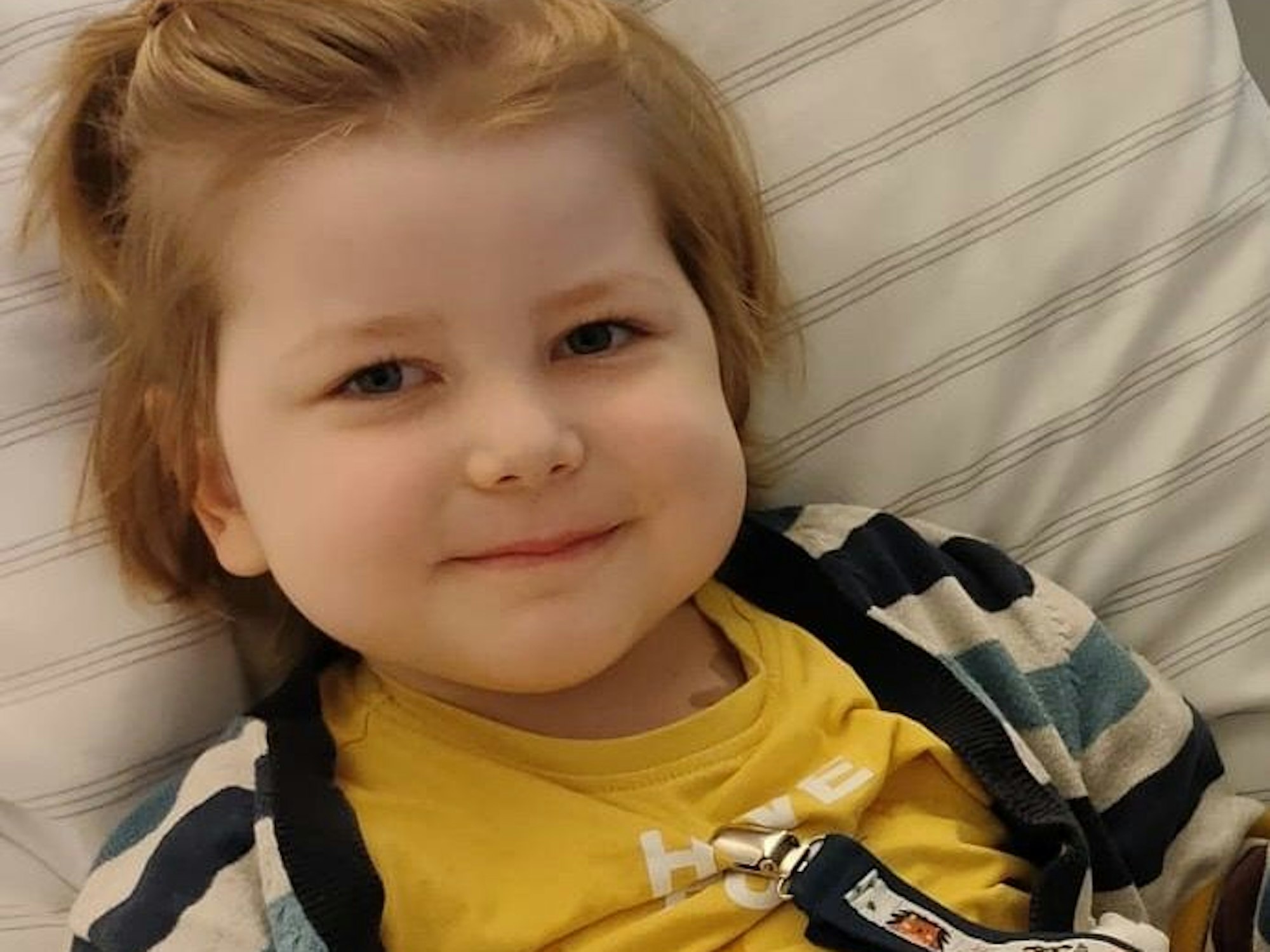 Ein kleiner Junge liegt im Bett und grinst.