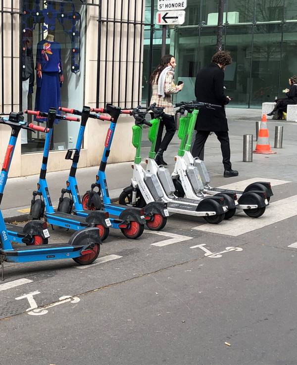 E-Scooter von drei verschiedenen Anbietern stehen auf einem dafür vorgesehenen Parkplatz.