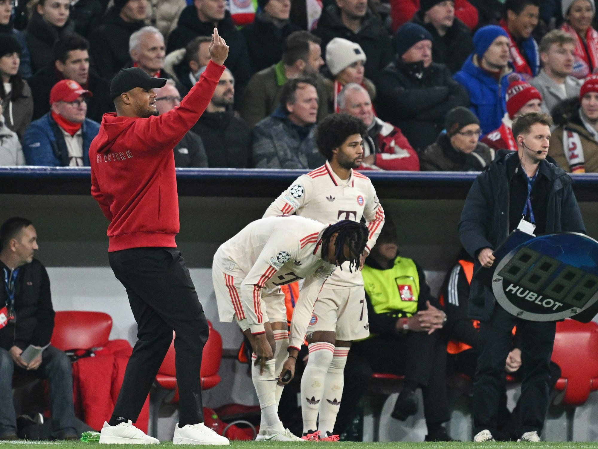 Münchens Trainer Vincent Kompany (l-r) gibt Anweisungen, während Michael Olise und Serge Gnabry zur Einwechslung bereitstehen.