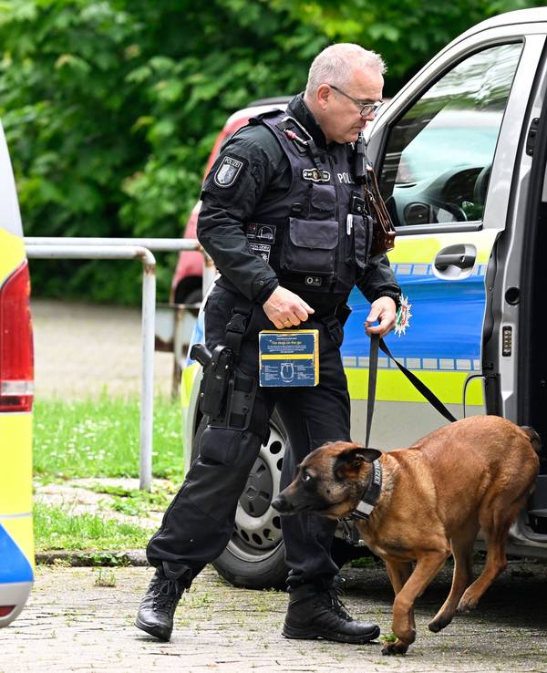 Ein Polizist hat einen Hund an der Leine, der aus einem Polizeifahrzeug springt.