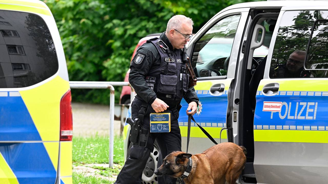 Ein Polizist hat einen Hund an der Leine, der aus einem Polizeifahrzeug springt.
