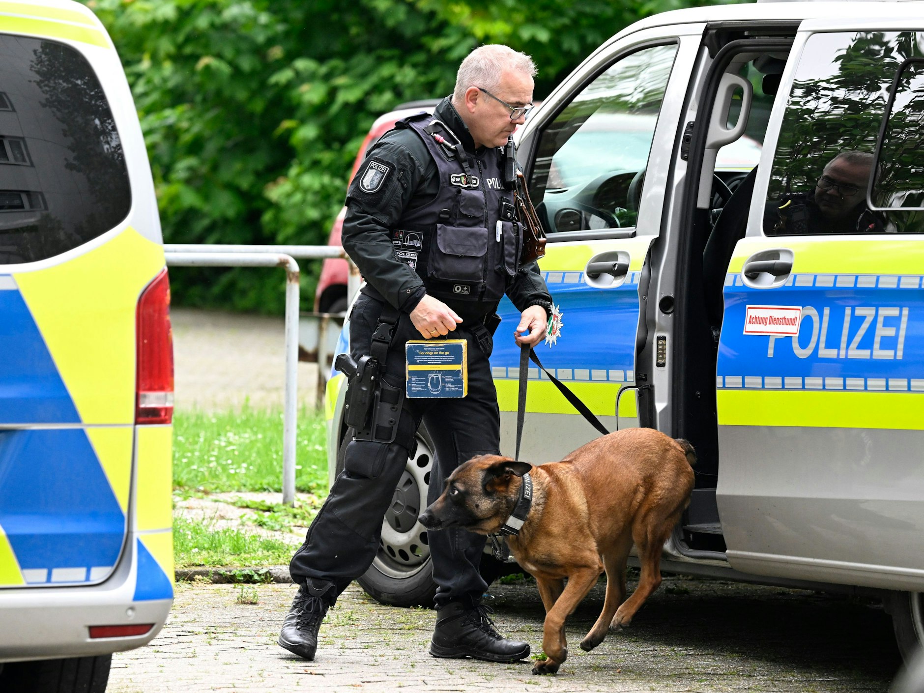Ein Polizist hat einen Hund an der Leine, der aus einem Polizeifahrzeug springt.