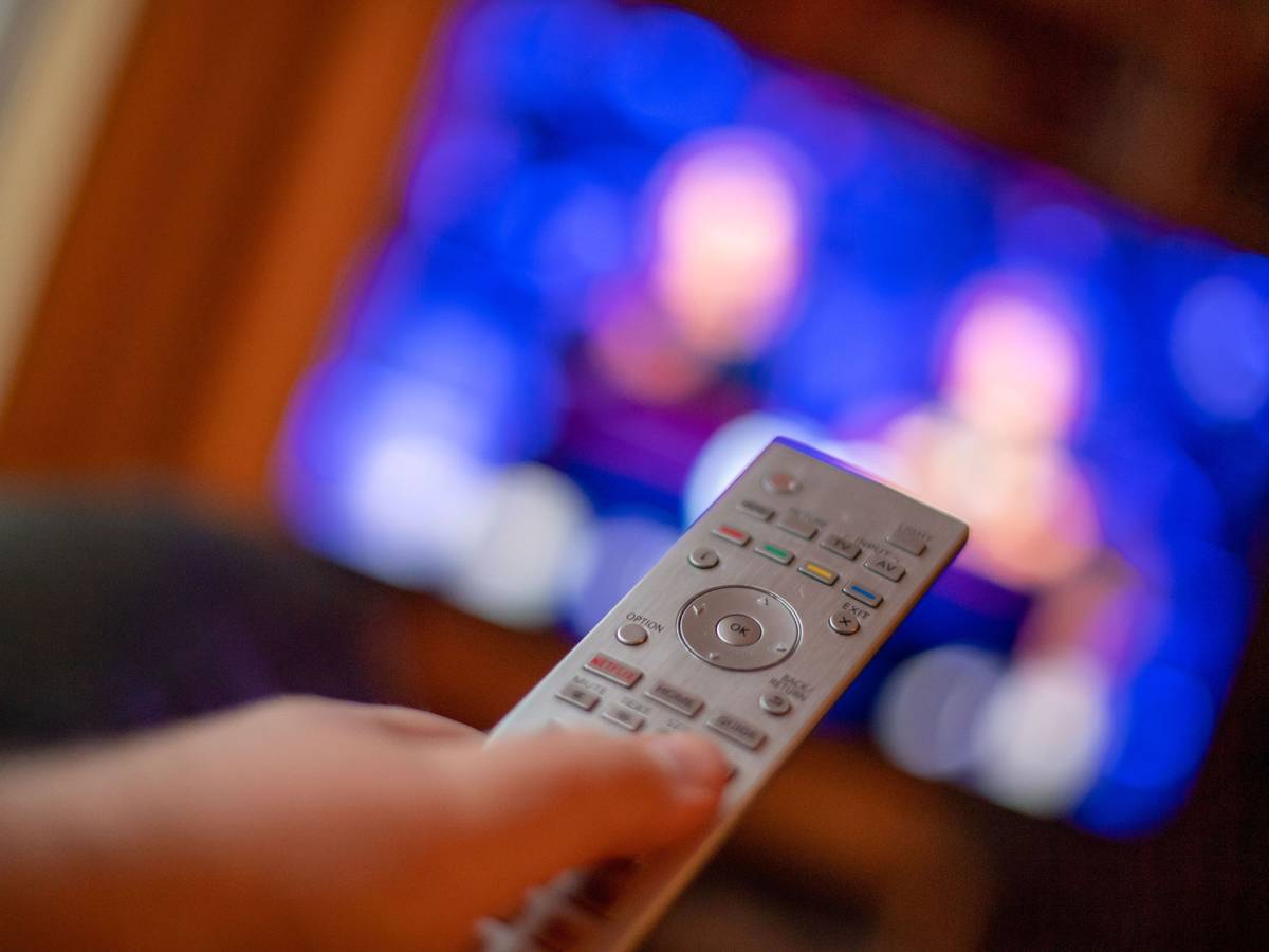 Ein Mann bedient mit der Fernbedienung einen Fernseher