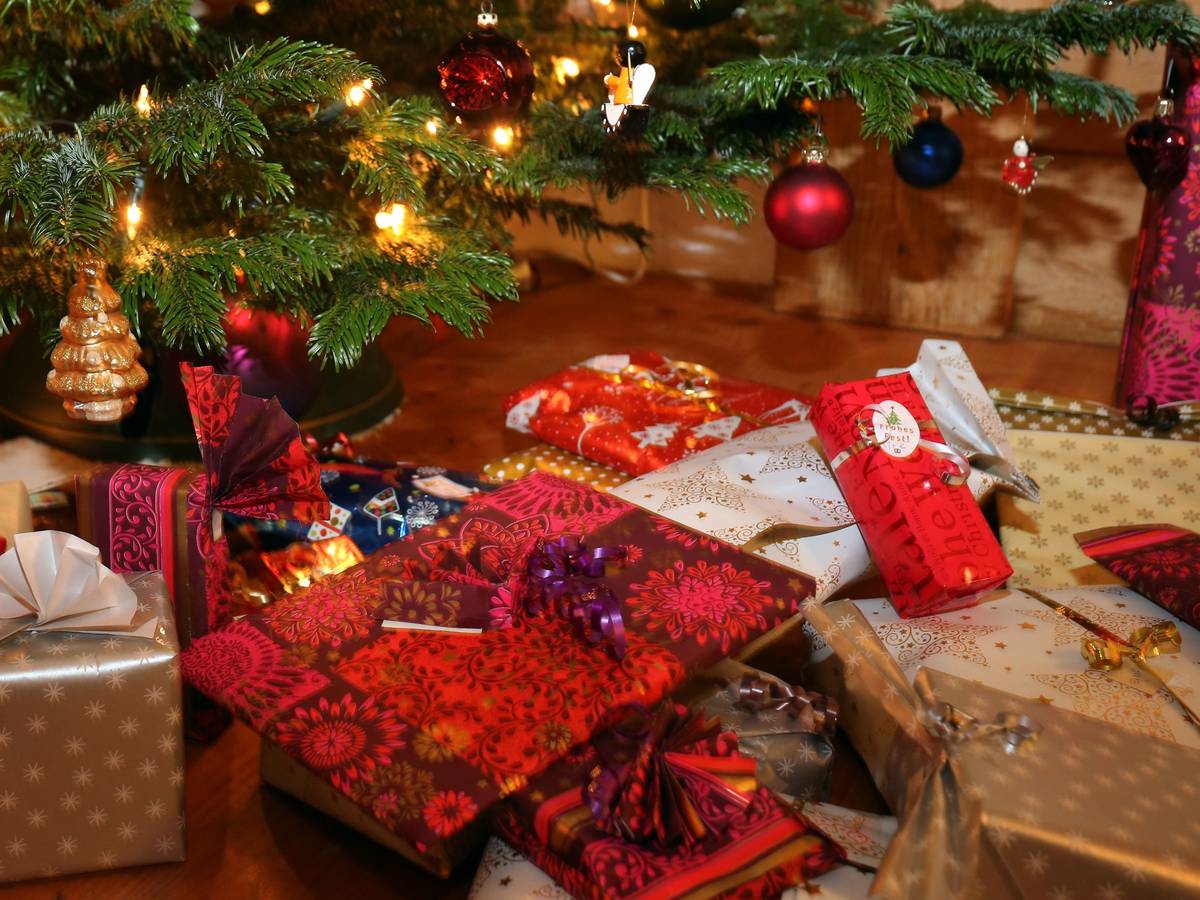 Verpackte Weihnachtsgeschenke liegen unter einem Christbaum.