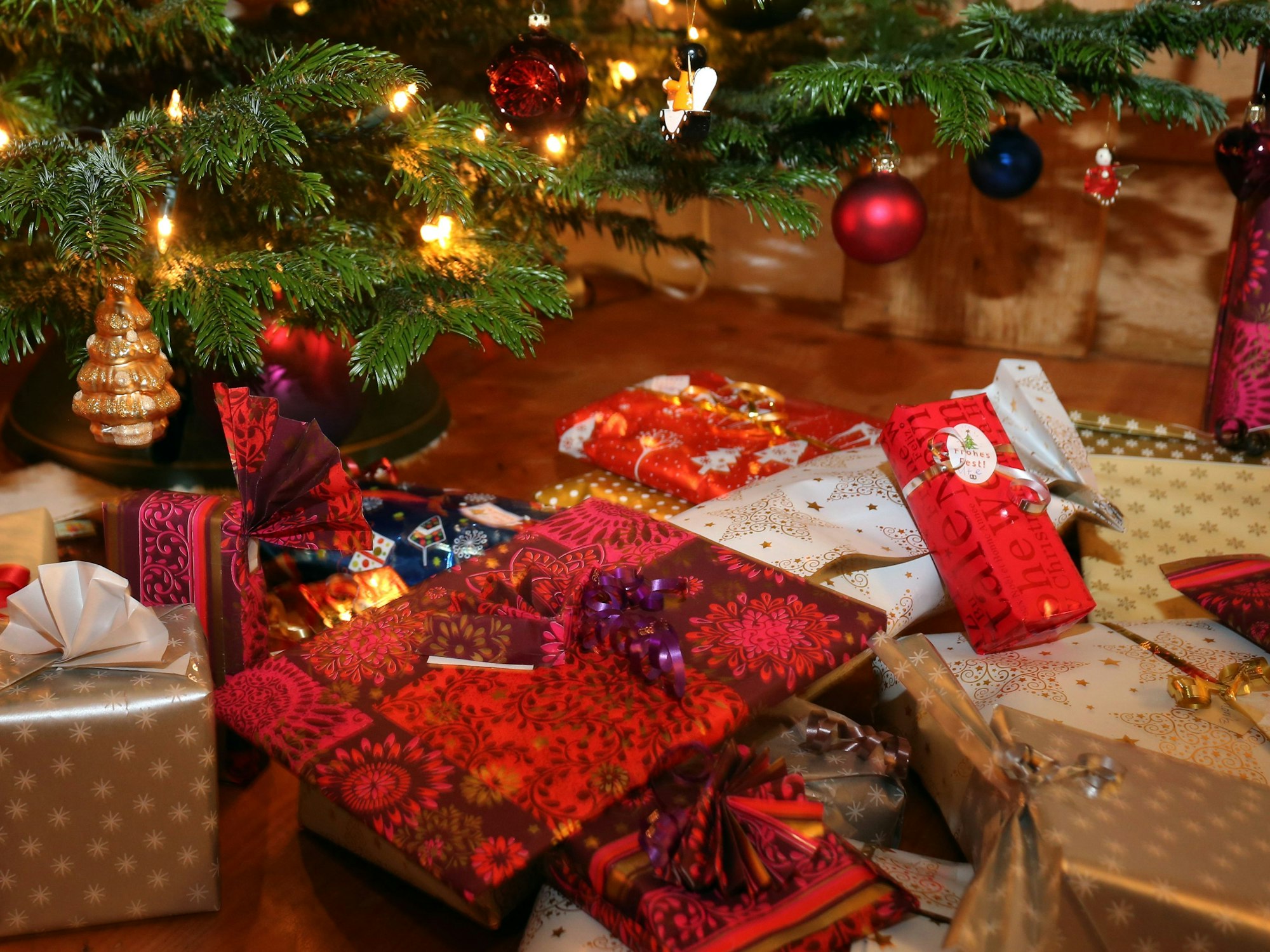 Verpackte Weihnachtsgeschenke liegen unter einem Christbaum.