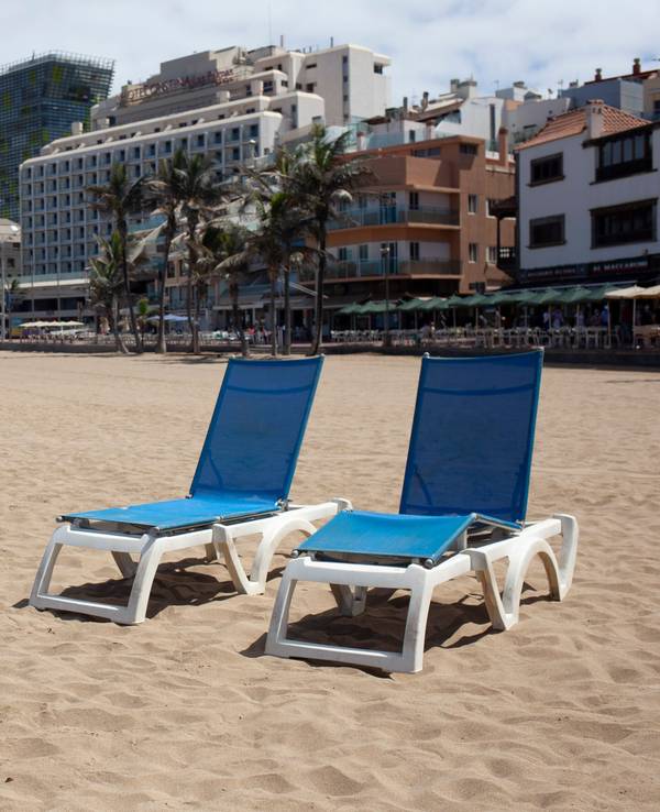 Vier Liegestühle am Strand von Las Canteras auf Gran Canaria stehen im Sand.