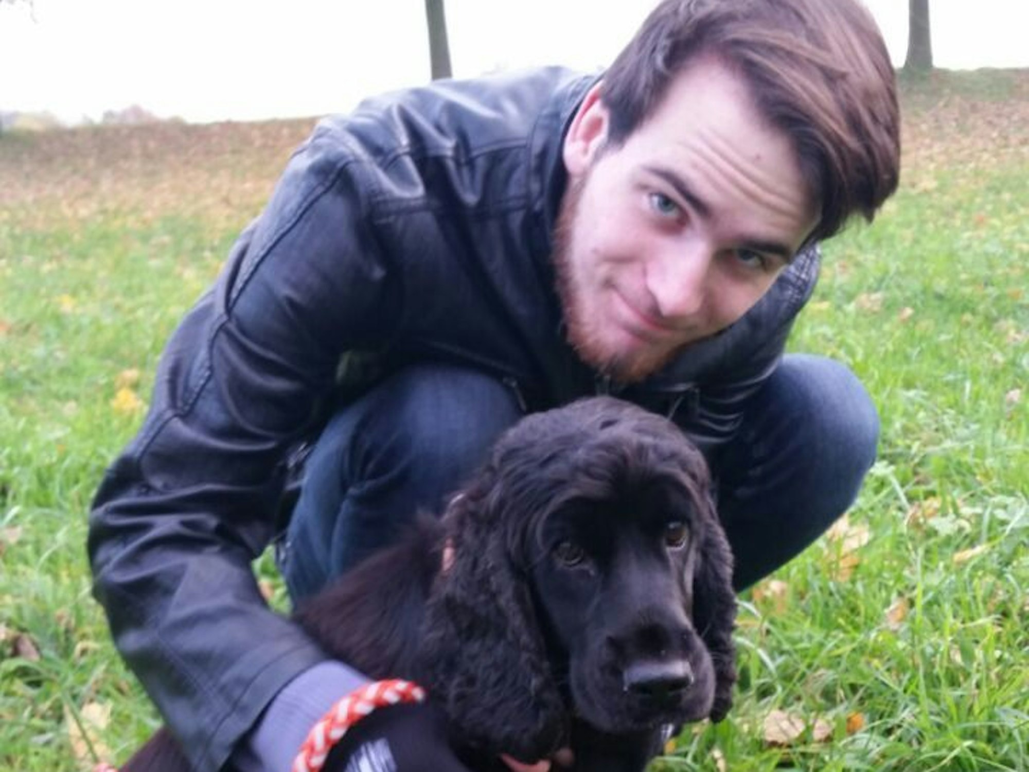 Ein Mann kniet mit einer Hündin auf einer Wiese.