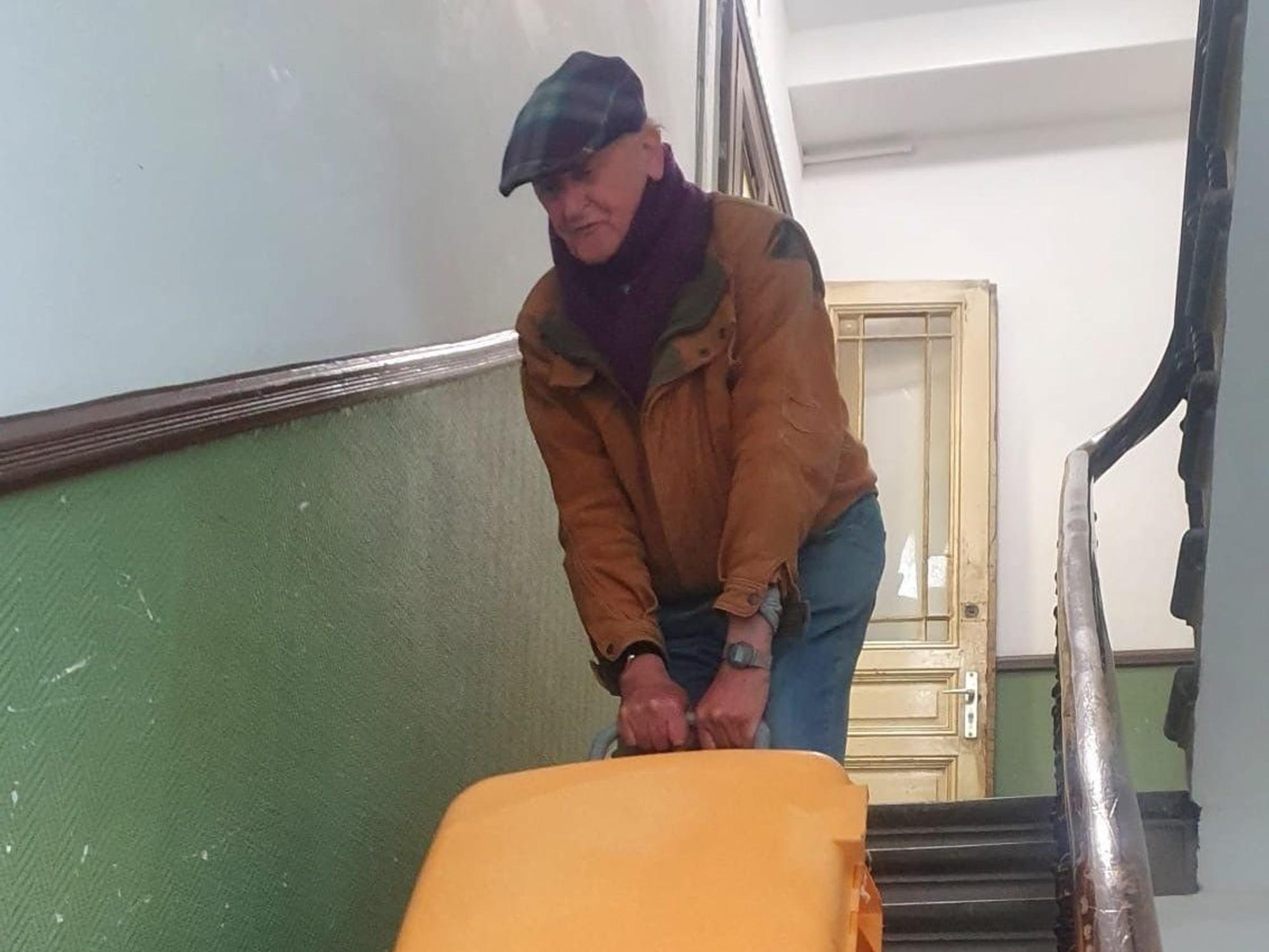 Ein alter Herr bringt einen Koffer die Treppen eines Treppenhauses hinunter.