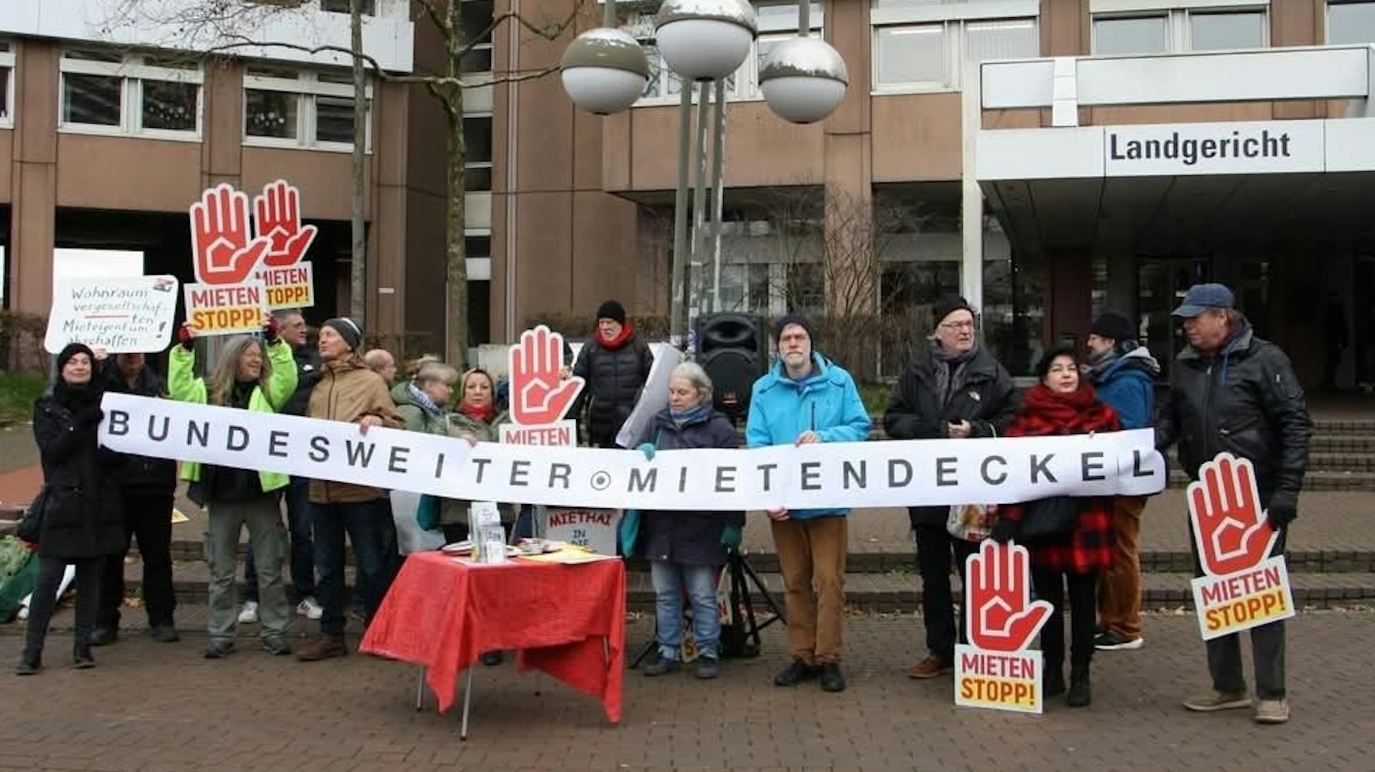 Menschen stehen vor dem Landgericht und halten ein Plakat mit der Aufschrift „Bundesweiter Mietendeckel“ vor sich.